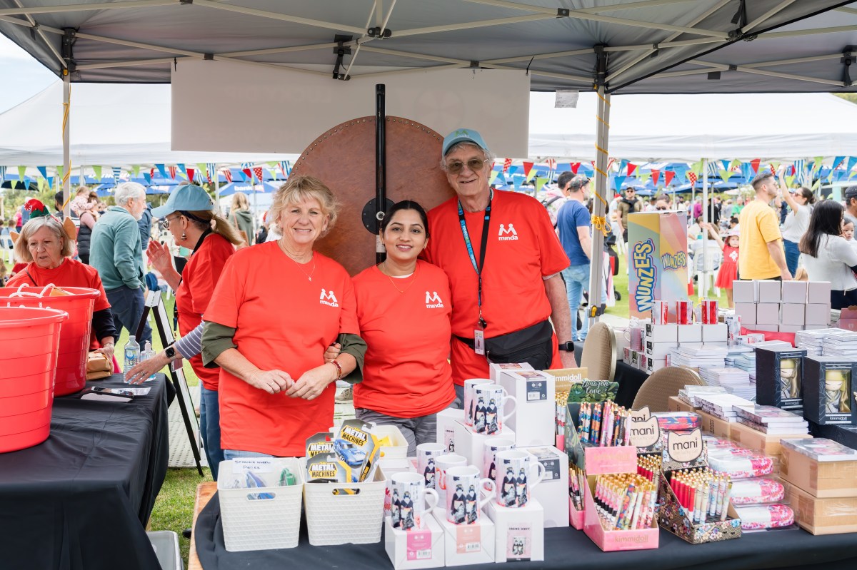 A group of volunteers in red shirts stand at a market stall, looking cheerful.