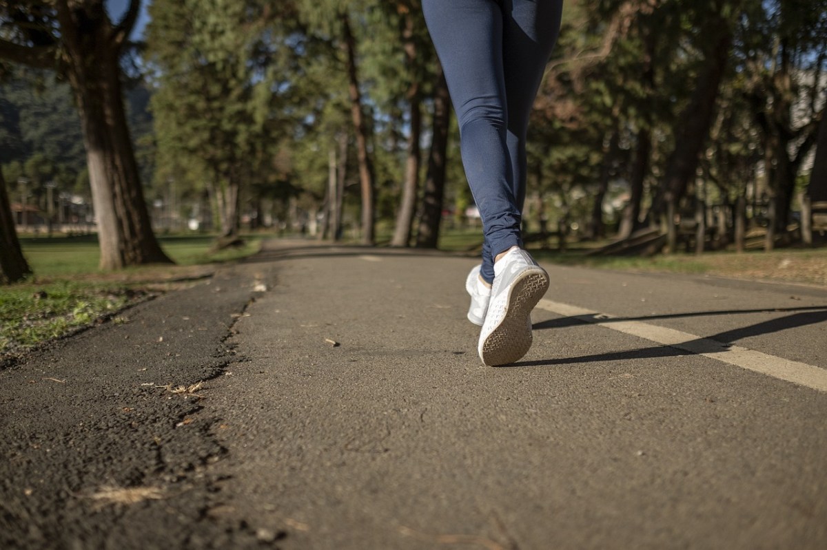 We see a foot in a white runner and blue leggings mid-stride, jogging through a park with trees.