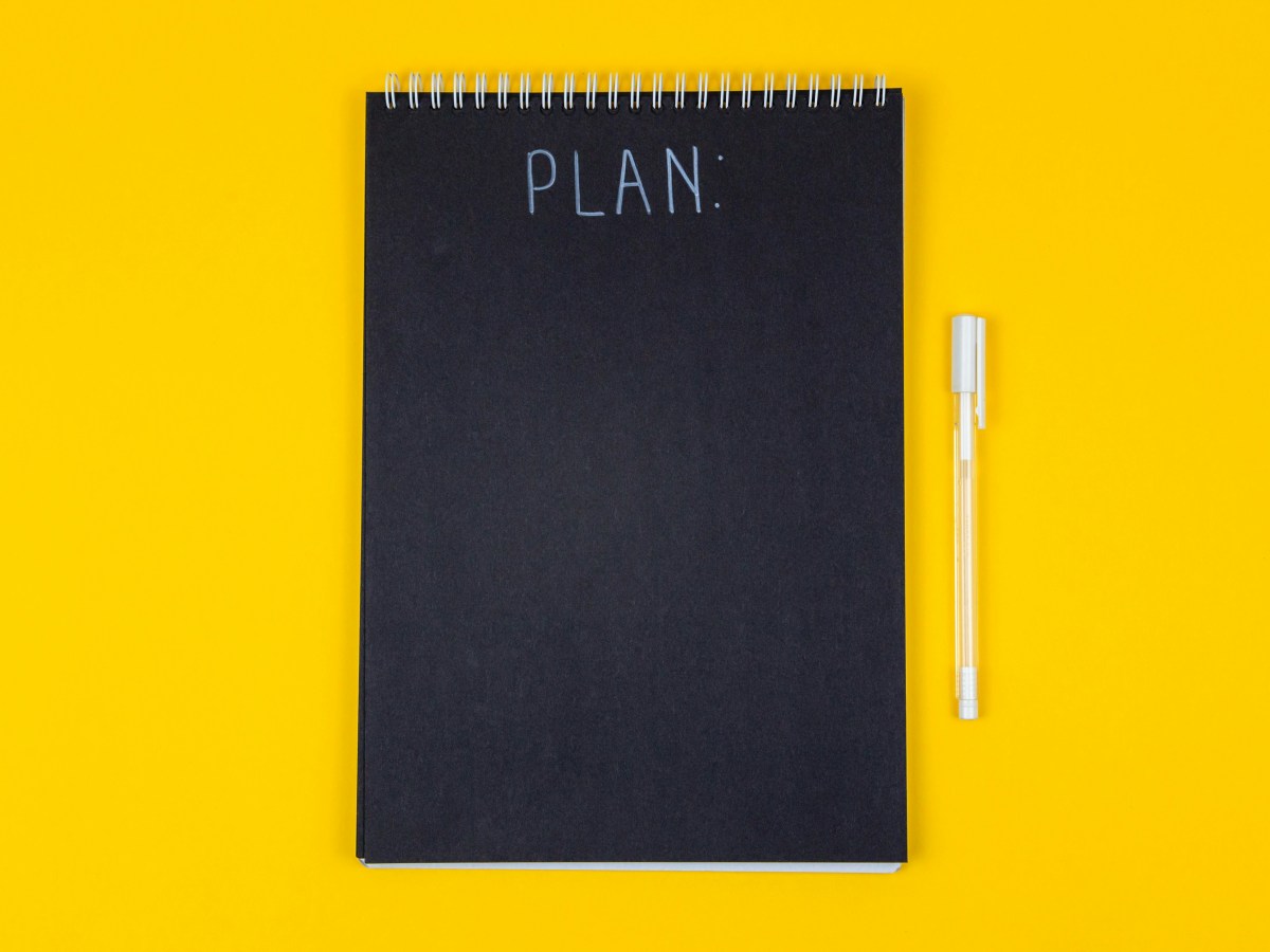 A black notepad on a yellow background with a white pen. The word 'plan' is written in white on the notepad at the top.