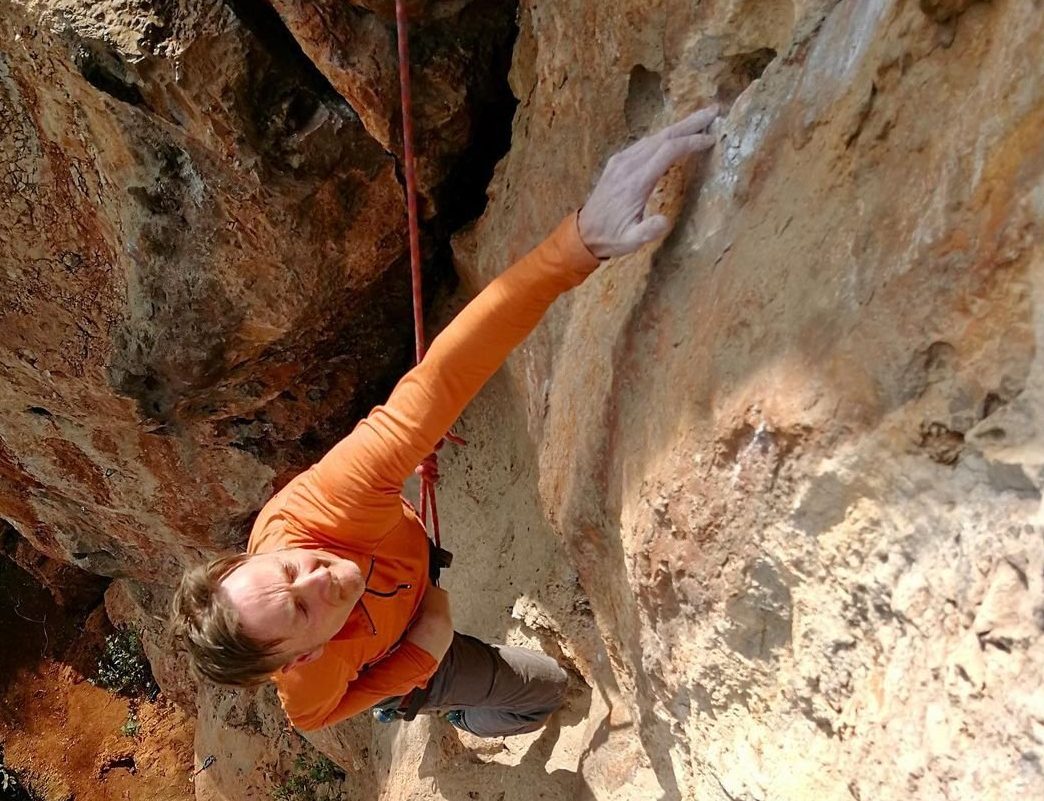 Paul Pritchard, a disabled man wearing orange, is climbing up a rock face.