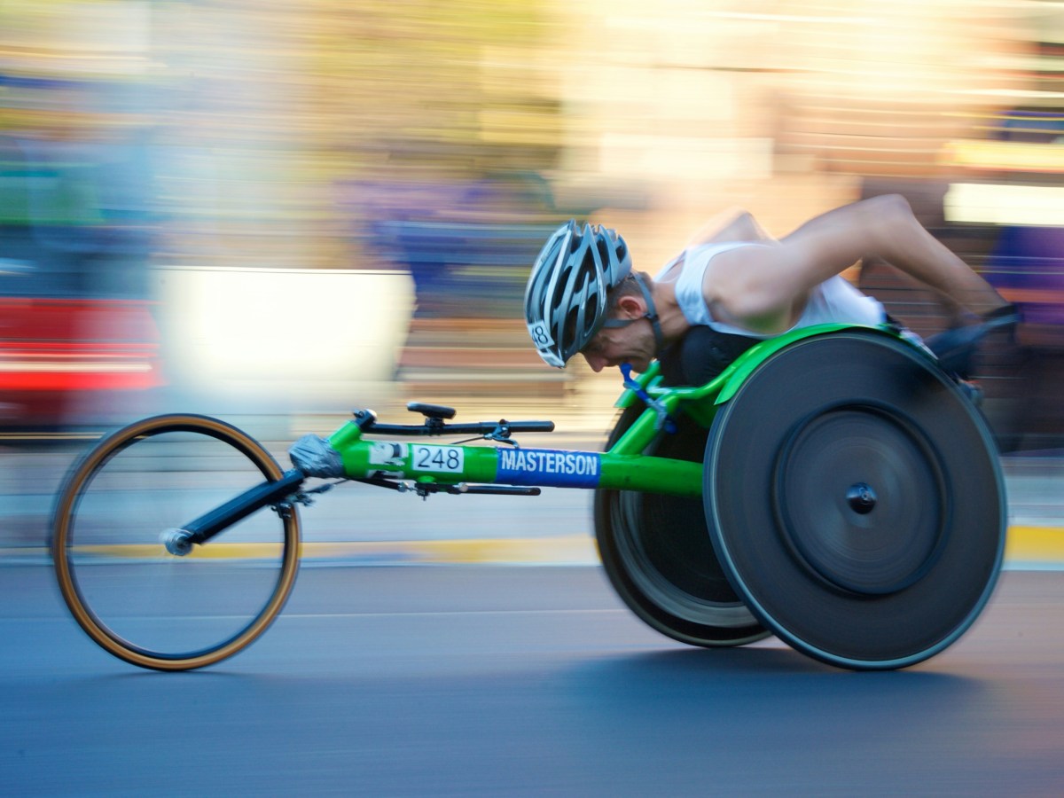 A para-athlete competing in wheelchair racing in a green wheelchair.