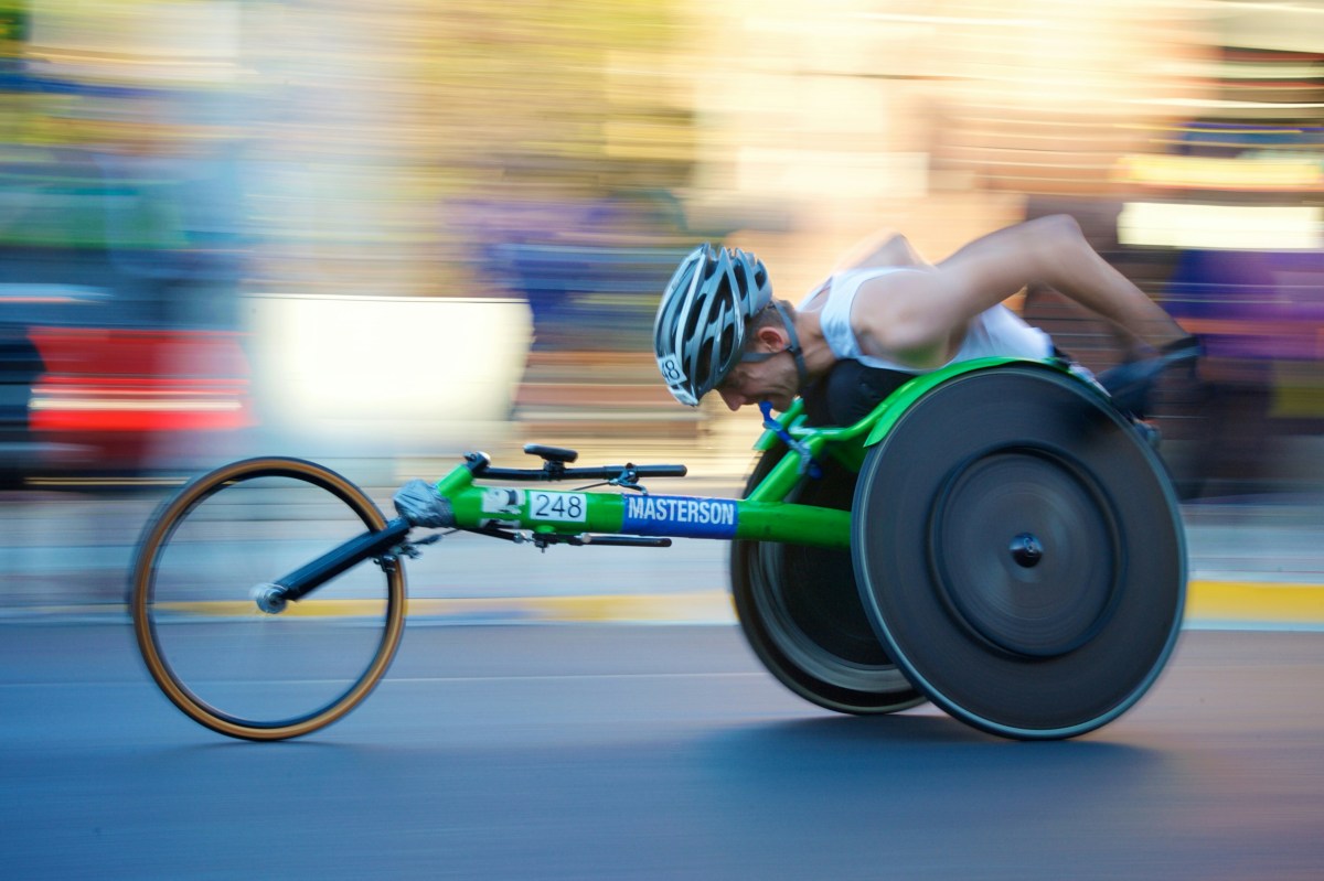 A para-athlete competing in wheelchair racing in a green wheelchair.