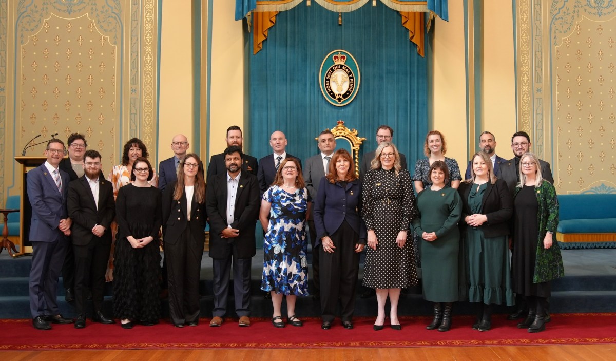 A group of people, all in suits and professional dress, stand for an official portrait on a red floor in front of a teal and yellow background.