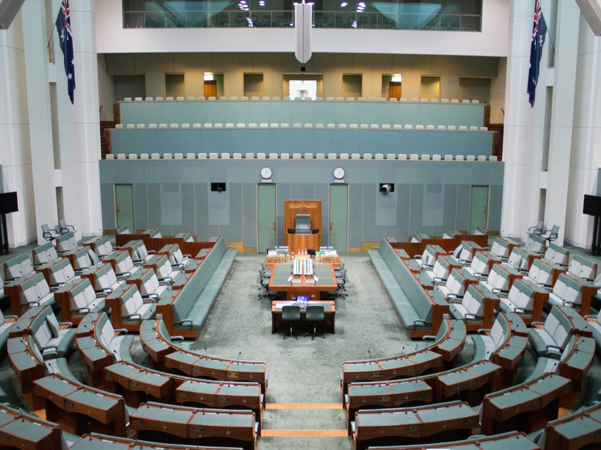 The green House of Representatives chamber in Australia's Parliament House, with lots of green chairs looking down at a long table in the centre.