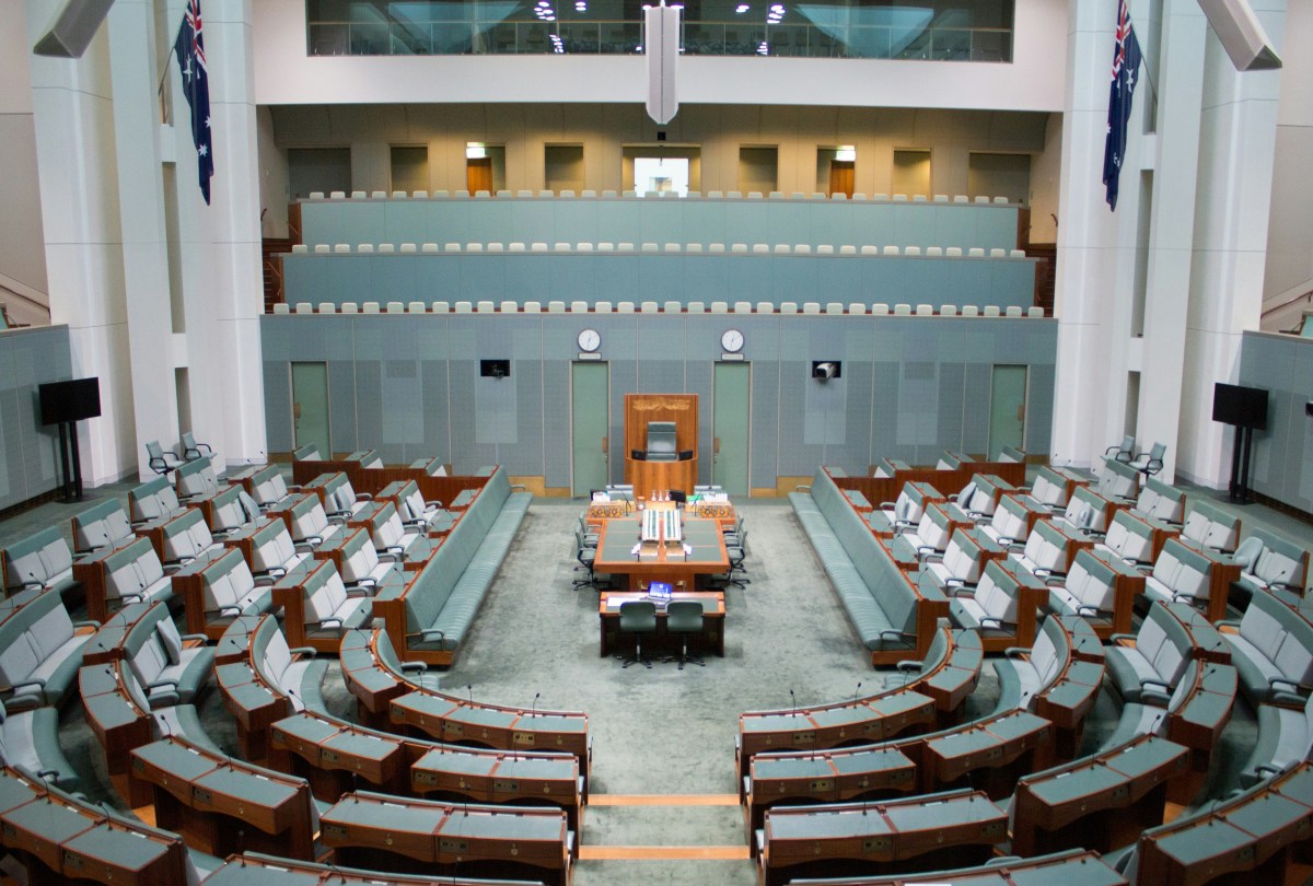 The green House of Representatives chamber in Australia's Parliament House, with lots of green chairs looking down at a long table in the centre.