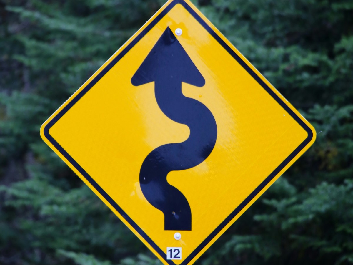 A yellow sign with a squiggly road arrow drawn on it.