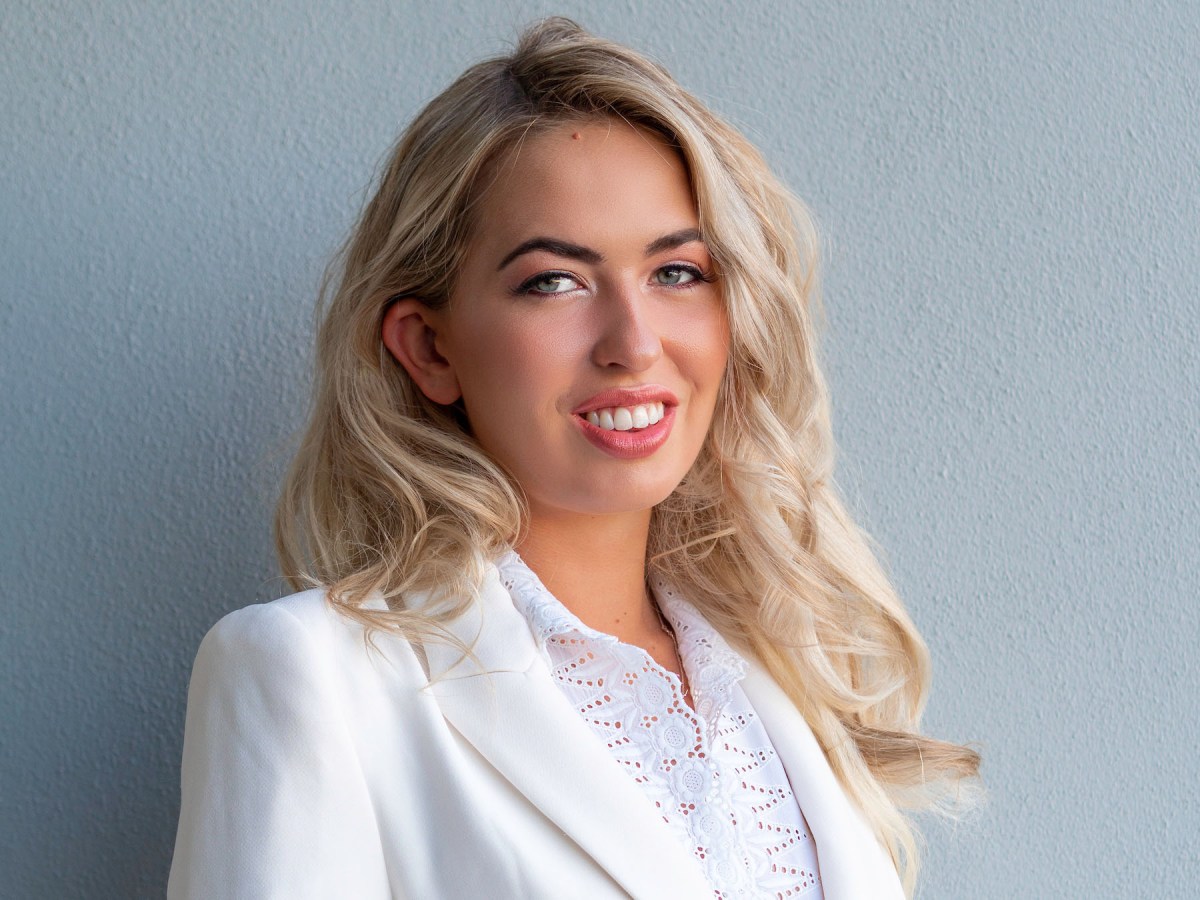 A headshot of Anja Christofferson, a young woman with long blonde hair wearing a white suit.