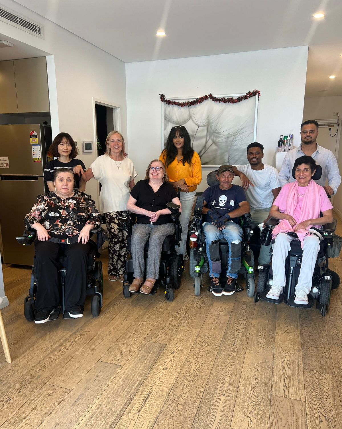 A group of people with visible disabilities, including several using wheelchairs, in a new house.