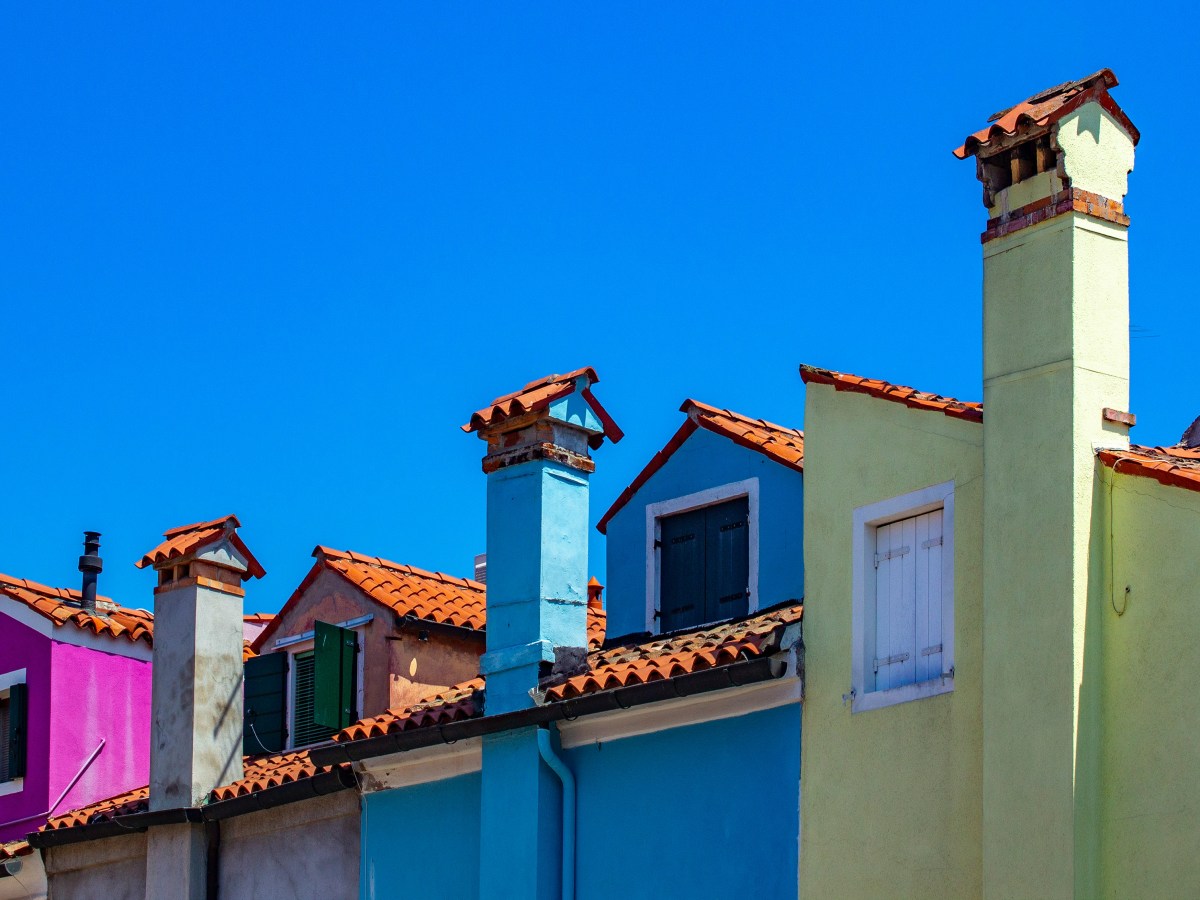 A row of connected houses in bright colours like pink, blue and green. We can only see the top of each house. The sky behind them is bright blue.