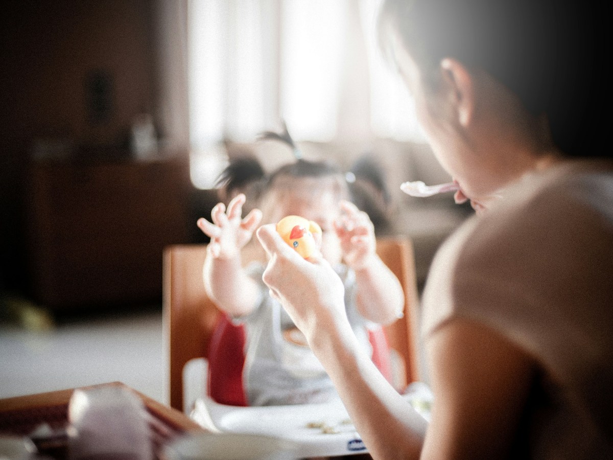 A mother feeding her baby a spoonful of food at the table, in an artistic blur.