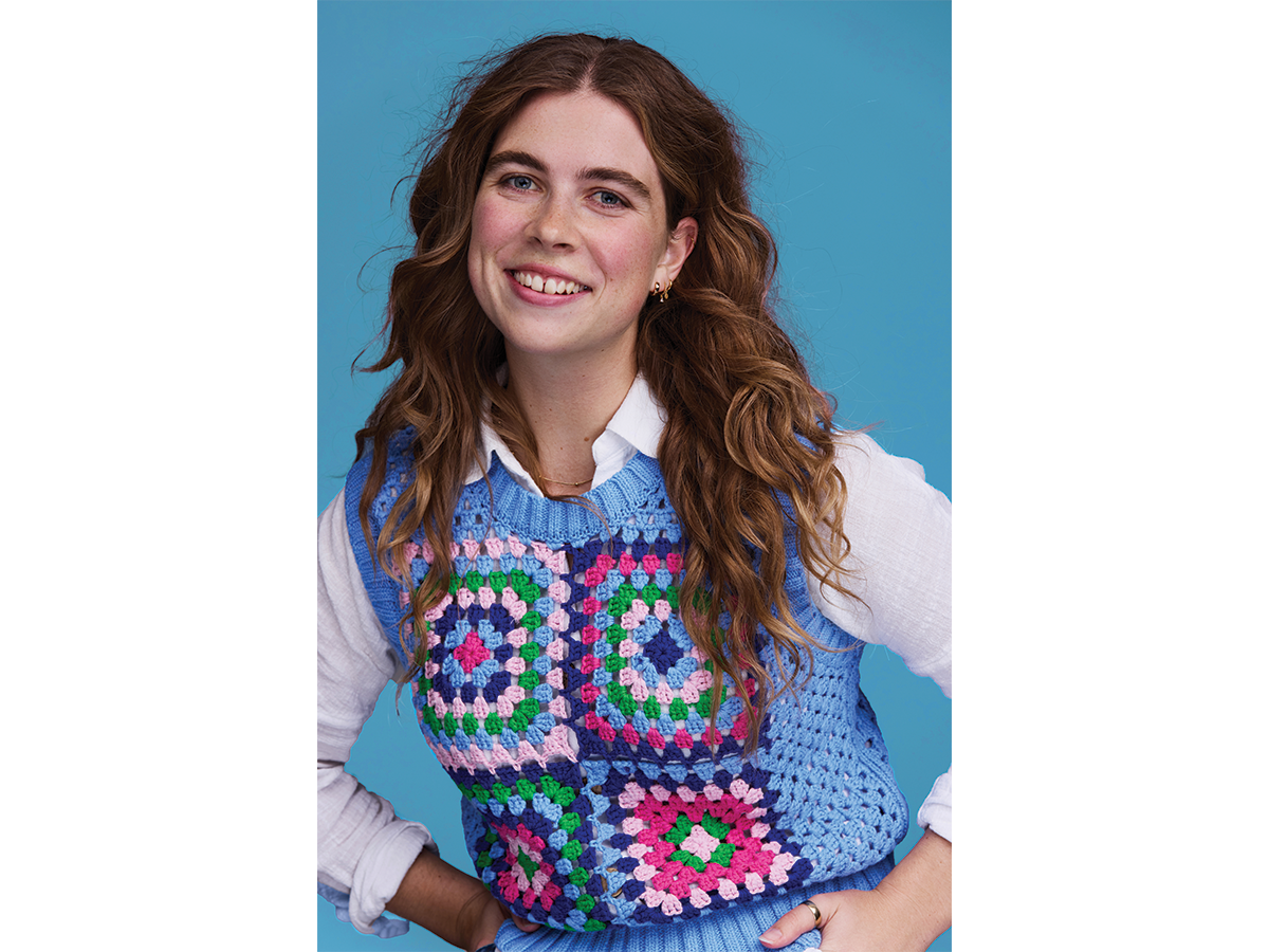 Filmmaker Lily Drummond, a young woman with long brown wavy hair, wearing a white shirt with a colourful crochet vest over the top.