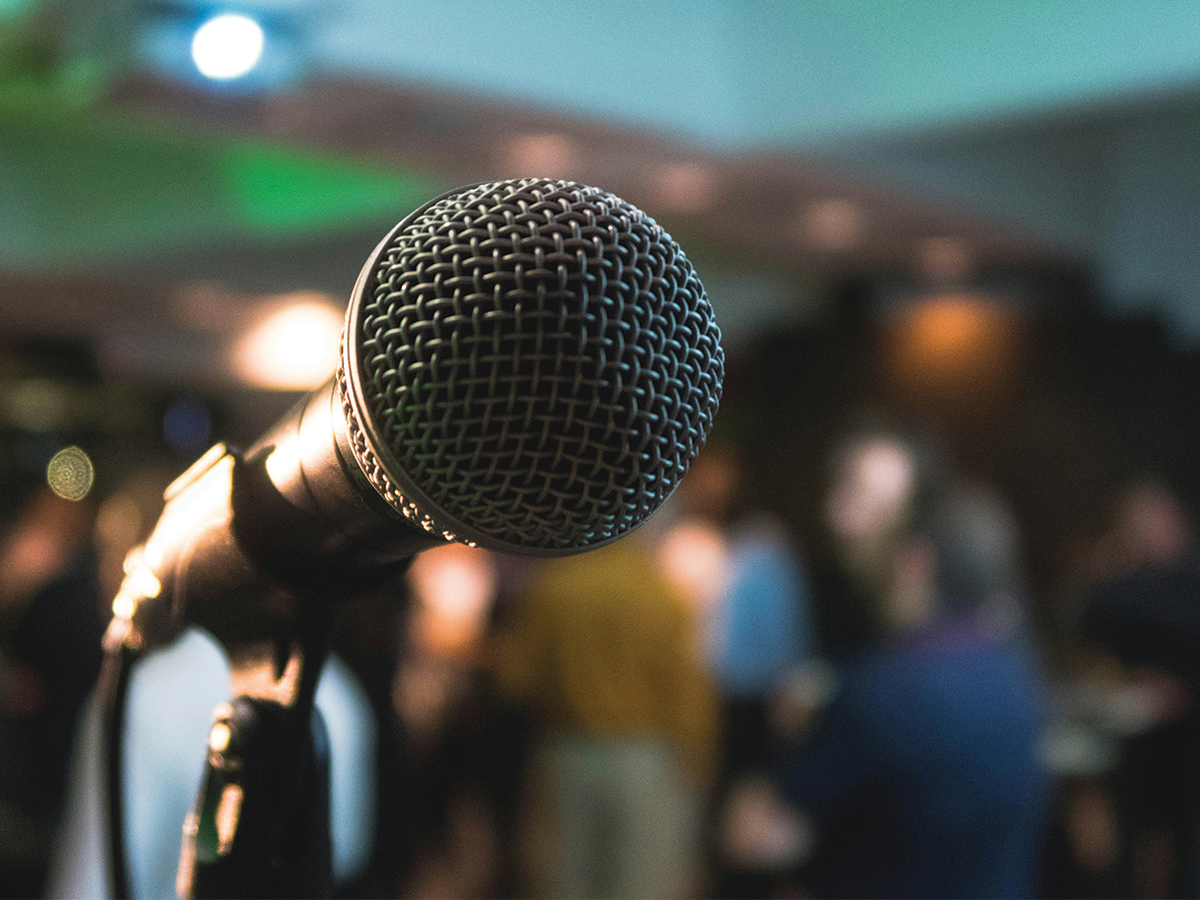 A microphone directly in front of the camera, with a blurred background that looks like people standing around.