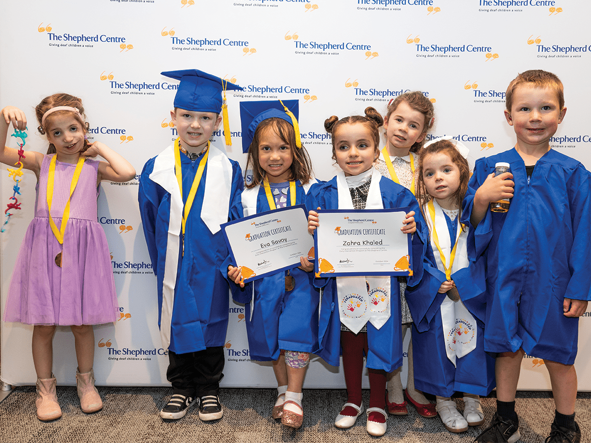 A group of young children, most in royal blue graduation robes. They are all very young.