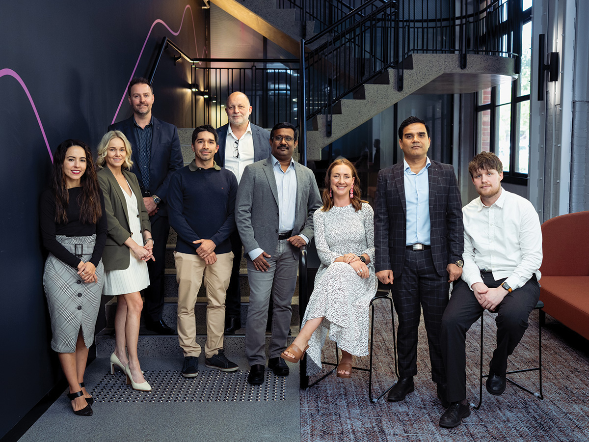 A group of people in professional clothes pose in a group, they are all smiling at the camera.