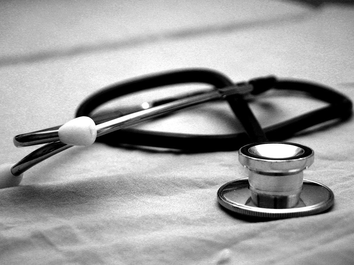 A stethoscope curled on a white surface. Photo is in black and white.